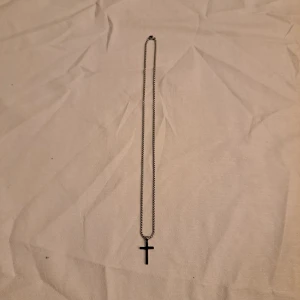 Silverfärgat halsband med kors - Stilrent halsband i silverfärg med en klassisk korsberlock. Kedjan är rundlänkad och har ett smidigt lås. Korset är slätt och minimalistiskt, vilket gör det lätt att matcha med olika outfits. Perfekt för dig som gillar enkla och snygga accessoarer.