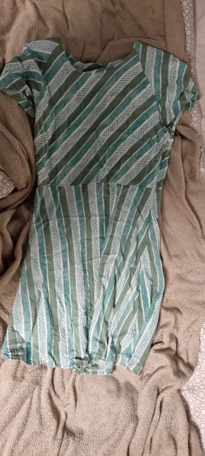 Grön och vit randig klänning Samsøe Samsøe - Snygg kortklänning från Samsøe Samsøe med grönt och vitt randigt mönster. Klänningen har korta ärmar och är tillverkad i mjuk bomull, perfekt för varma dagar. Den har en avslappnad passform och ett lekfullt mönster som sticker ut.