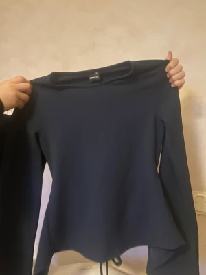 Mörkblå långärmad topp Gina Tricot XS - Snygg mörkblå långärmad topp från Gina Tricot i storlek XS. Modellen har en croppad passform med snörning i midjan som ger en cool detalj. Materialet känns mjukt och stretchigt, perfekt för dig som gillar stilrena och enkla plagg med en twist.