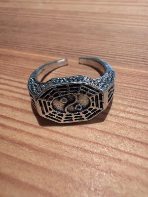 Silvrig ring med yin yang-symbol - Unik silvrig ring med en oktagonal form och detaljerat yin yang-motiv i centrum. Ringen har graverade mönster runt om som ger en cool och mystisk vibe. Perfekt för dig som gillar asiatiska influenser och vill sticka ut med din stil.