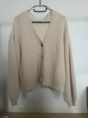Beige stickad kofta med knappar - Vila - Säljer en beige stickad kofta med grov struktur och mörka knappar framtill från Vila.   Obs: Alla plagg säljs endast fram till 28/12 