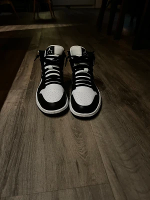 Nike Air Jordan 1 svart/vit sneakers - Säljer ett par Nike Air Jordan 1 sneakers i svart och vitt. Klassisk high-top modell med snörning, rund tå och platt sula. Skorna har ikoniska Air Jordan-loggan på sidan och Nike Swoosh. Tillverkade i skinn med svart yttersula och perforerad tå för extra ventilation. Den har används max 2 gånger som du kan se