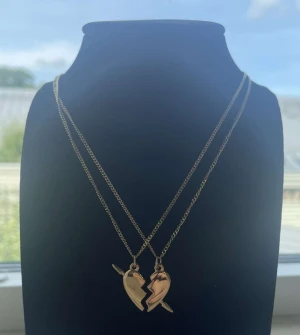 Guldiga halsband med krossade hjärtan - Två guldiga halsband med matchande hängen som tillsammans bildar ett brustet hjärta. Perfekt för dig och din bästa vän! Kedjorna är tunna och eleganta, och hjärthängena har en cool, delad design med pil-detalj. Snygg accessoar som sticker ut. Rostfri 