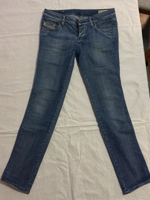 Blå Diesel Cuddy jeans W28 L32 - Snygga blå Diesel Cuddy jeans med klassisk femficksdesign och knäppning med knappar. Jeansen har en lätt tvättad look och stretchigt material för extra komfort. Perfekta för dig som gillar en stilren och avslappnad vibe.