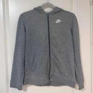 Grå kofta med dragkedja - Grå kofta med dragkedja från Nike med vit logga på bröstet. Koftan har huva och fickor framtill