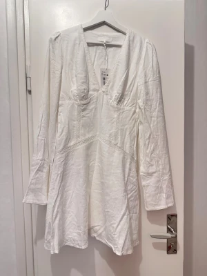 Vit spetsdetaljerad miniklänning - Superfin vit klänning med v-ringning och långa ärmar. Klänningen har spetsdetaljer längs sömmarna och är tillverkad i ett luftigt linnematerial. Perfekt för skolavslutning eller student. Helt oanvänd med lapparna kvar! Skicka gärna pm för prisförhandling eller frågor☺️