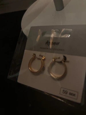 Guldpläterade hoops från Appear - Snygga små hoop-örhängen i guldpläterad metall från Appear. De har en klassisk rund form med diskret räfflad yta som ger lite extra edge. Perfekta för dig som gillar stilrena accessoarer med en twist.