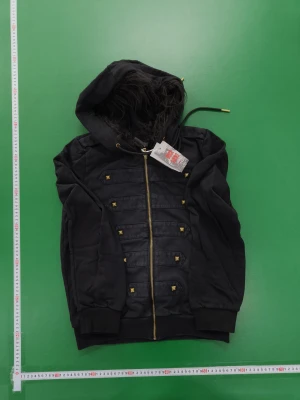 Svart bomberjacka y2k med huva och nitar - Svart bomberjacka med huva och fluffigt foder, detaljerad med guldfärgade nitar och dragkedja framtill. Jackan har snörning i huvan och ribbade muddar vid ärmslut och nederkant. Snygg militärinspirerad look med flera dekorativa band på framsidan.