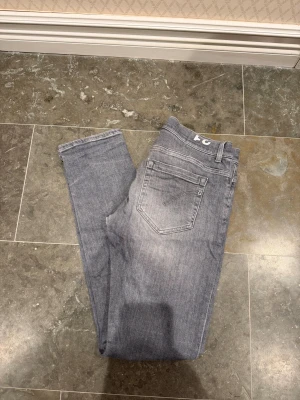 Grå skinny jeans från Dondup - Snygga grå Dondup George jeans, Skinny Fit. De har klassisk femficksdesign, smal passform och är tillverkade i mjukt bomullsmaterial med lite stretch. Perfekt för dig som gillar en modern och stilren look. Den svarta Dondup badgen sitter lite löst på ena sidan men det ser man nästan inte alls,  Vid några frågor eller funderingar är det bara att höra av dig och fråga på🤩
