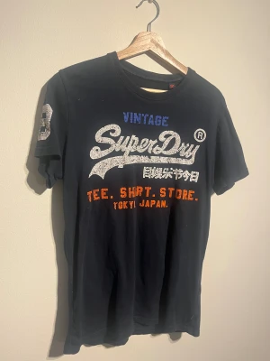 Superdry T-Shirt - Hej! Säljer nu denna väldigt snygga Superdry T-Shirten. Storlek M Medium   Färg: Mörkblå Skick: Gott, väl använd med i fint skick.  Skickas spårbart eller hämtas upp efter överenskommelse. Vid intresse – hör gärna av dig.  Skriv vid frågor eller ifall du vill ha fler bilder:) 