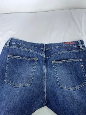 Blå jeans från Dondup, Made in Italy - Snygga blå jeans från Dondup med klassisk femficksdesign och coola slitningar framtill. Jeansen har raka ben, normal passform och detaljer som metallogo på bakfickan och röd kontrastsöm vid linningen. Tillverkade i robust denim för en tidlös look.