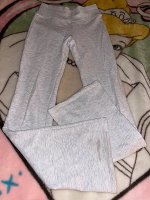 Ljusgrå bootcut mjukisbyxor - Säljer ett par ljusgrå mjukisbyxor med bootcut-ben och hög midja. Byxorna är tillverkade i mjukt bomullsmaterial och har en bred, ribbad linning för extra komfort. Perfekta för chill dagar eller när du vill ha en avslappnad look.