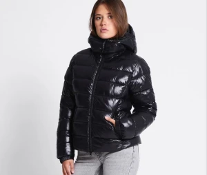 Svart glansig pufferjacka med huva - Säljer en svart, glansig pufferjacka med huva och dragkedja framtill. Jackan har en quiltad look med breda kanaler och är perfekt för kalla dagar. Den har lång ärm och en lite boxig passform som ger en cool vibe. Den är lite figursydd och säljs pågrund av fel storlek. Använd 1 gång. 