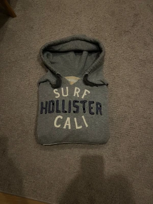 Hollister hoodie  - Jag säljer nu min sjukt eftertraktade hollister hoodie, hoodien är i storlek L men jag skulle säga att storleken M beskriver den bättre! Slitningar på hoodien är gjorde i fabrik och detta är en väldigt cool hoodie. Jag köpte den för 1200kr men säljer den för endast 850kr      !!!PRIS KAN SÅKLART DISKUTERAS!!!
