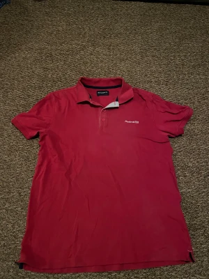 Röd pikétröja från Reebok Originals - Röd pikétröja från Reebok Originals med klassisk krage och knappar framtill. Tröjan har Reebok-logga på bröstet och är tillverkad i mjuk bomull. Perfekt för en sportig och avslappnad stil.