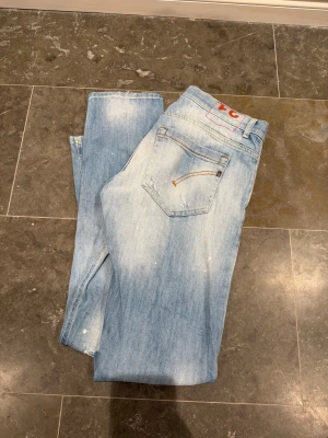 Ljusblå skinny jeans från Dondup - Säljer ett par helt sprillans nya ljusblå Dondup George jeans. Jeansen har slitna detaljer, diskreta färgstänk och klassisk femficksdesign. De är tillverkade i mjukt denim med snygg tvätt och passar perfekt för en trendig streetstil. Har du några frågor eller funderingar så är det bara att höra av sig🤩