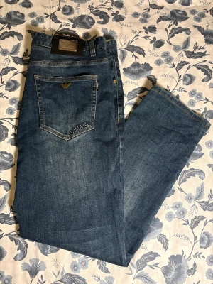 Armani Jeans  - Snygga blå jeans från Armani med klassisk femficksdesign och guldfärgad logga på bakfickan. Jeansen har raka ben och normal passform, med broderad Armani-text på bakfickan och detaljerade sömmar. Perfekt för dig som gillar stilrena och exklusiva jeans. Priset kan diskuteras!