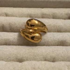Guldfärgad chunky ring  - Snygg chunky ring i guldfärg med två droppformade ändar som möts framtill. Ringen har en modern och unik design som sticker ut och passar perfekt för dig som gillar statement-smycken. Perfekt att matcha med andra guldsmycken för en cool look.