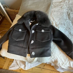 Grå kappa med pälskrage från Meotine - Säljer en snygg grå jacka från Meotine Charlie i storlek XS/ S. Endast använd en gång. Den har en lyxig pälskrage och stora fickor framtill. Perfekt för höst och vinter! Jackan är i mycket bra skick och har en stilren design med knappar framtill. Nypris 3500. Mitt pris. 2000 