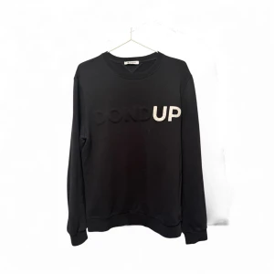 Svart sweatshirt från Dondup - Svart sweatshirt från Dondup med stor logotyp i svart och silver på bröstet. Tröjan har rund hals, ribbade muddar och lång ärm. Tillverkad i mjuk bomull, perfekt för en chill och stilren look.
