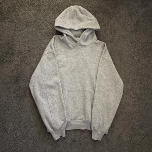 Grå hoodie från Junkyard i storlek M - Säljer en stilren grå hoodie från Junkyard i storlek M. Tröjan har en klassisk huva, ribbade muddar och en loose passform. Materialet är mjuk bomull med insida i fleece som gör den extra skön. Perfekt för chill dagar och streetwear-vibe.