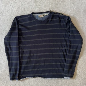 Randig marinblå tröja med knappar - Säljer en marinblå och grårandig tröja med rund hals och tre snygga knappar på axeln. Tröjan har lång ärm och är tillverkad i mjuk bomull, perfekt för en chill och stilren look. Storlek S/M