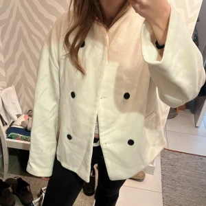 Oversized jacka med dubbelknäppning - Snygg oversized jacka med dubbelknäppning och svarta knappar. Rak passform, utan krage och med fickor på sidorna. Från Hanna schönbergs kollektion. Vet inte storlek men passar nog S-L