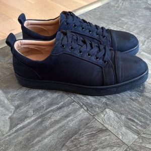 Loubs - Snygga svarta sneakers från Christian Louboutin med klassisk röd sula och broderad logga på hälen. Skorna har rund tå, snörning och är tillverkade i mocka med mjukt beige foder. Perfekt för dig som gillar exklusiv streetstyle. Priset kan diskuteras