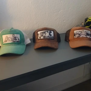 Maggiore kepsar med retrofoto - Tre snygga kepsar från Maggiore med klassiska svartvita fototryck framtill. En keps är mintgrön och vit, en är brun och en är ljusbrun, alla med mesh på sidorna och baksidan. Materialet är mockaliknande framtill och polyester mesh bak. Perfekt för dig som gillar unik stil.