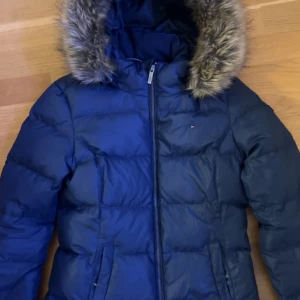 Vinterjacka Tommy Hilfiger - Säljer en mörkblå pufferjacka från Tommy Hilfiger med huva och päls. Jackan har dragkedja framtill, två fickor och diskret logga på bröstet och ärmen. nypris 2700