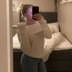 Offshoulder stickad tröja i vitt - Säljer en superfin offshoulder stickad tröja i vitt med bred ribbad kant upptill. Tröjan har lång ärm och en snygg, lite loose passform. Perfekt att styla med jeans eller kostymbyxor för en trendig look.