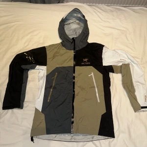 Arc'teryx x Beams vindjacka M - Säljer en Arc'teryx Beams vindjacka i färgblockad design med svart, grå, beige och vit. Jackan har huva, dragkedja framtill och två snedställda fickor med dragkedja. Materialet är lätt och tekniskt, perfekt för utomhusaktiviteter. Broderad Arc'teryx-logga på bröstet. Bara använd ett fåtal gånger, inget som syns! Hör av er vid frågor😁