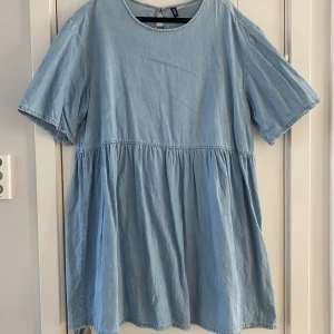 Ljusblå kort klänning från H&M Divided - Supersöt ljusblå klänning från H&M Divided i storlek L. Modellen är kort med rund halsringning och korta ärmar. Tillverkad i 100% bomull, vilket gör den mjuk och skön. Klänningen har en avslappnad passform och ett rynkat midjeparti som ger en chill vibe. Mått Över bröstet: ca 59 cm Längd från axeln och ner: ca 94 cm  100% bomull  Kommer från ett djur och rökfritt hem.