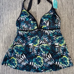 Blommig bikini med halterneck från MyWear - Snygg bikini från MyWear i storlek XL med tropiskt blommigt mönster i blått, grönt, gult och vitt. Modellen har halterneck med knyt i nacken och lätt utställd form nedtill. Materialet är mjuk och stretchig polyester med elastan för skön passform. Perfekt för strandhäng! Mått Över bröstet: ca 41 cm  Polyester och elastan  Kommer från ett djur och rökfritt hem.