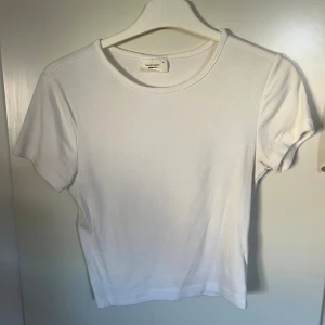 Vit basic topp från Gina Tricot - En klassisk vit basic topp från Gina Tricot, Basically Basics-kollektionen. T-shirten har rund halsringning och korta ärmar. Tillverkad i mjuk bomull för en skön känsla och enkel stil. Perfekt att matcha med allt i garderoben.