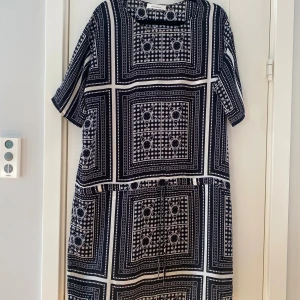 Svartvit kortklänning med grafiskt mönster - Säljer en svartvit kortklänning med grafiskt rutigt mönster och coola detaljer. Klänningen har korta ärmar och snörning i midjan för en snygg passform. Materialet är mjukt och lätt, perfekt för dig som gillar statement-plagg med unik design. Mått Över bröstet: ca 63 cm Över höften: ca 57 cm Längd från axeln och ner: ca 97 cm  Polyester  Kommer från ett djur och rökfritt hem.