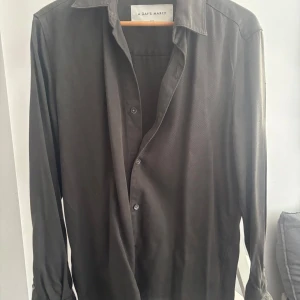 Oliv grön skjorta från A Day's March - Stilren oliv grön skjorta från A Day's March i storlek small. Skjortan har klassisk krage, knäppning framtill och långa ärmar. Materialet känns mjukt och har en lätt glans, vilket ger en snygg look. Perfekt för dig som gillar minimalistisk stil.