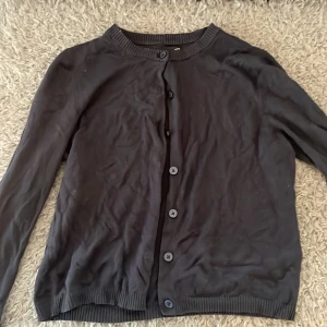 Mörkblå kofta från 157, storlek S - En mörkblå, klassisk kofta från 157 i storlek S. Koftan har rund halsringning, långa ärmar och knäppning med fem knappar framtill. Ribbstickade muddar vid ärmslut och nederkant ger en snygg finish. Perfekt att slänga över en t-shirt eller linne.