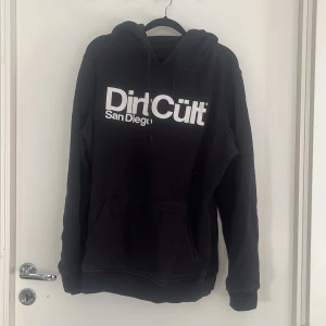 Svart dirtcült hoodie - Säljer en svart dirtcült hoodie då den inte kommer till användning. Har en känguruficka i fram, hoodie med snörning. Inga defekter vad jag har sätt.