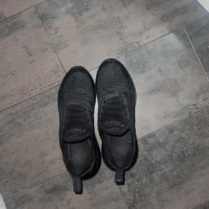 Svarta Nike Air Max 270 sneakers - Säljer ett par svarta Nike Air Max 270 sneakers med chunky sula och mesh-överdel. Skorna har en modern design med rund tå och synlig Air-enhet i hälen. Perfekta för dig som gillar sportig stil och vill ha bekväma sneakers med cool look.