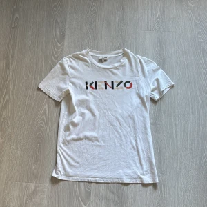 Vit Kenzo t-shirt med logga - Snygg vit t-shirt från Kenzo med färgglad logga framtill. Klassisk rund halsringning och korta ärmar. Tillverkad i mjuk bomull som känns skön mot huden. Perfekt för dig som gillar stilrena plagg med en twist.