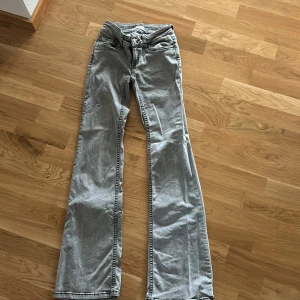 Ljusgrå bootcut jeans från Nelly - Säljer ett par ljusgrå jeans från Nelly med bootcut-modell. Jeansen har klassisk femficksdesign, hög midja och är tillverkade i jeansmaterial. Snygga kontrastsömmar och broderade bakfickor ger extra stilpoäng.