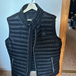 Svart dunväst från Moose Knuckles - Säljes då den inte används. Endast använd 2 gånger, dessa säljs inte längre har jag för mig men dem gick på typ 6000 ny. Stor i storlek 