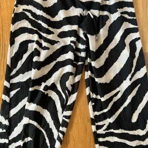 Zebramönstrade vida byxor - Snygga byxor med svartvitt zebramönster och vida ben. Perfekta för dig som vill sticka ut med en cool och trendig look. Byxorna har en lös passform och är tillverkade i ett lätt material som ger skön känsla hela dagen.