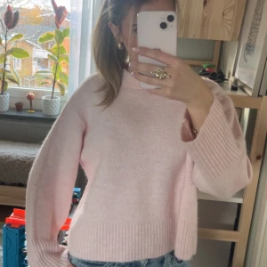 Ljusrosa stickad tröja med breda ärmar - Supermysig ljusrosa stickad tröja med breda, ribbade muddar vid ärmslut och nederkant. Tröjan har en rak passform och hög halsringning, perfekt att matcha med jeans för en chill look.