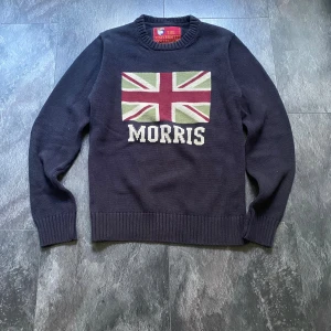 Stickad Morris Tröja - Hej! Säljer en väldigt snygg mörkblå stickad tröja från Morris. Tröjan har en patch på vardera armbåge och är i storlek M. Längden är 62 cm, armhåla till armhåla är tröjan 48 cm när tröjan ligger platt. Tröjan har även en snygg union jack flagga på framsidan och passar perfekt nu när vädret börjar bli kyligare. Hör av dig vid frågor eller funderingar!