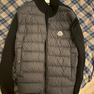 Moncler cardigan - Snygg svart quiltad jacka från Moncler med dragkedja och broderad logga på bröstet. Jackan har långa ärmar och en stilren design som passar perfekt för kyligare dagar. Köpt på Room1006 i Malmö, KVITTO FINNS! Storlek M, moncler galge på köpet