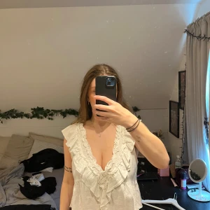 Vit blus med volanger från Gina Tricot - Superfin vit blus från Gina Tricot med djup v-ringning och volanger både fram och bak. Blusen är ärmlös och har en luftig, loose passform. Materialet är mjuk bomull och skön till sommaren.