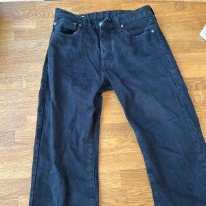 Levi's 501 svarta jeans W31 L32 - Svarta Levi's 501 jeans med klassisk rak passform och fem fickor. Jeansen har knappgylf, tydlig läderpatch bak och är tillverkade i robust denim. Perfekta för dig som gillar en tidlös och clean look.