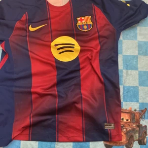 FC Barcelona Lamine Yamal tröja S - Säljer en FC Barcelona matchtröja från Nike med Lamine Yamal och nummer 10 på ryggen. Tröjan är kortärmad, har klassiska blå och röda ränder, gult Nike-märke och Spotify-logga på bröstet. Materialet är Dri-Fit polyester, perfekt för fotboll och träning.